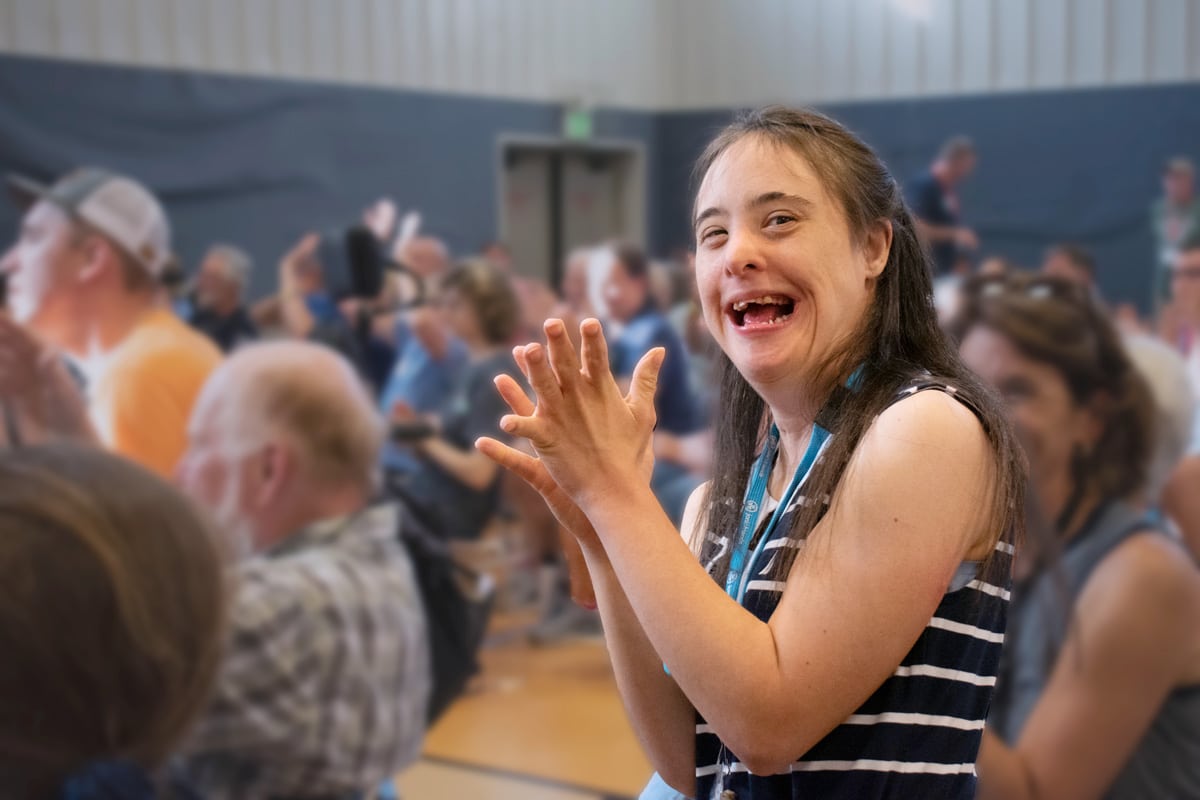 A young woman who appears to have down-syndrome smiling at the camera and clapping during a church service.