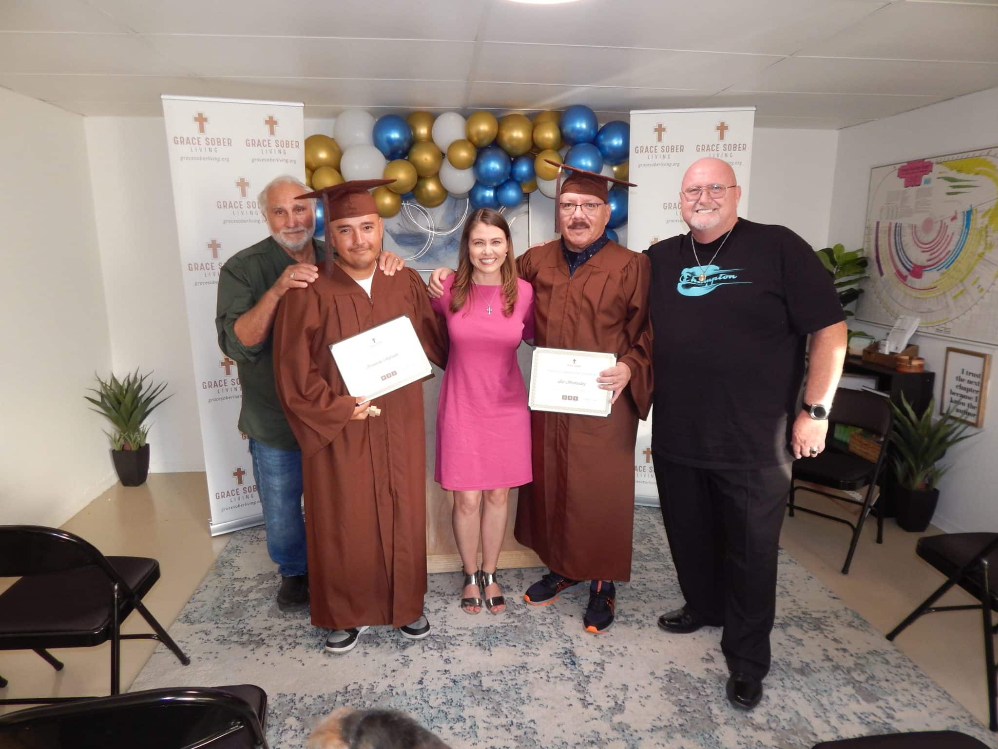 Jennifer standing with two graduates of the Grace Sober program and their family members.