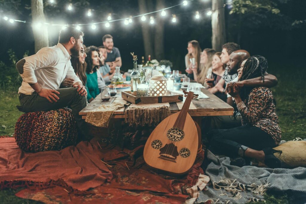 A group of people talking and smiling as they share a meal together under beautiful string lights.