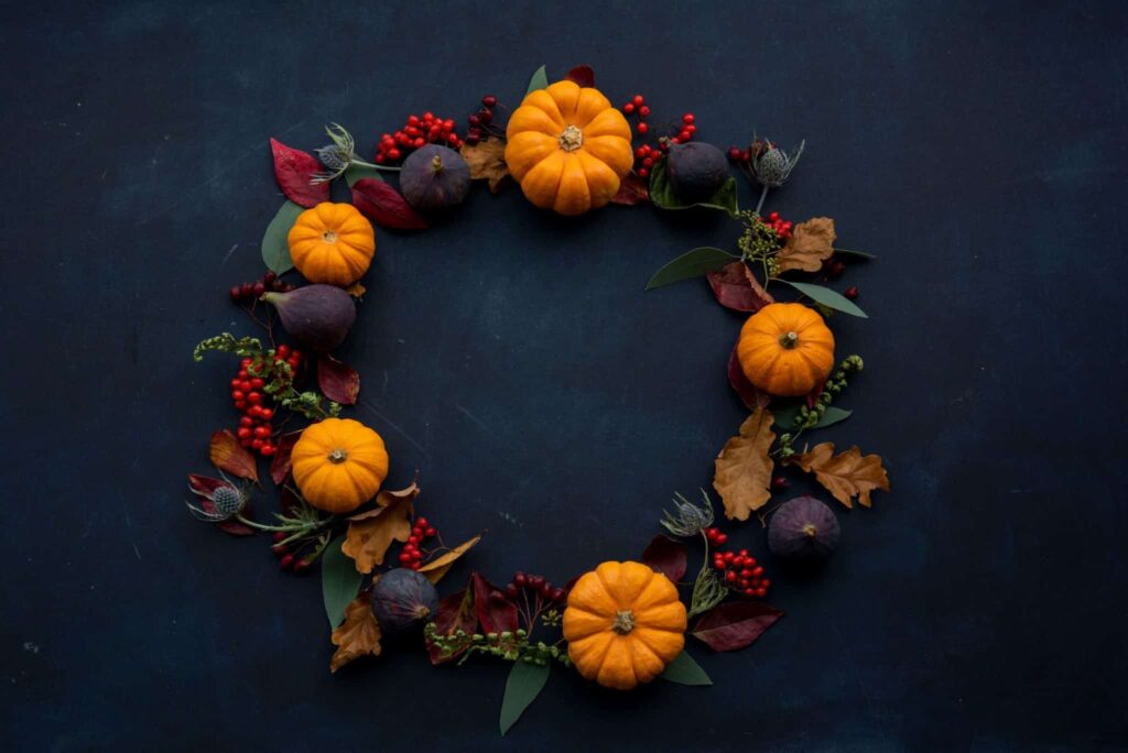 A dark blue table with pumpkins and leaves arranged in a wreath on it.
