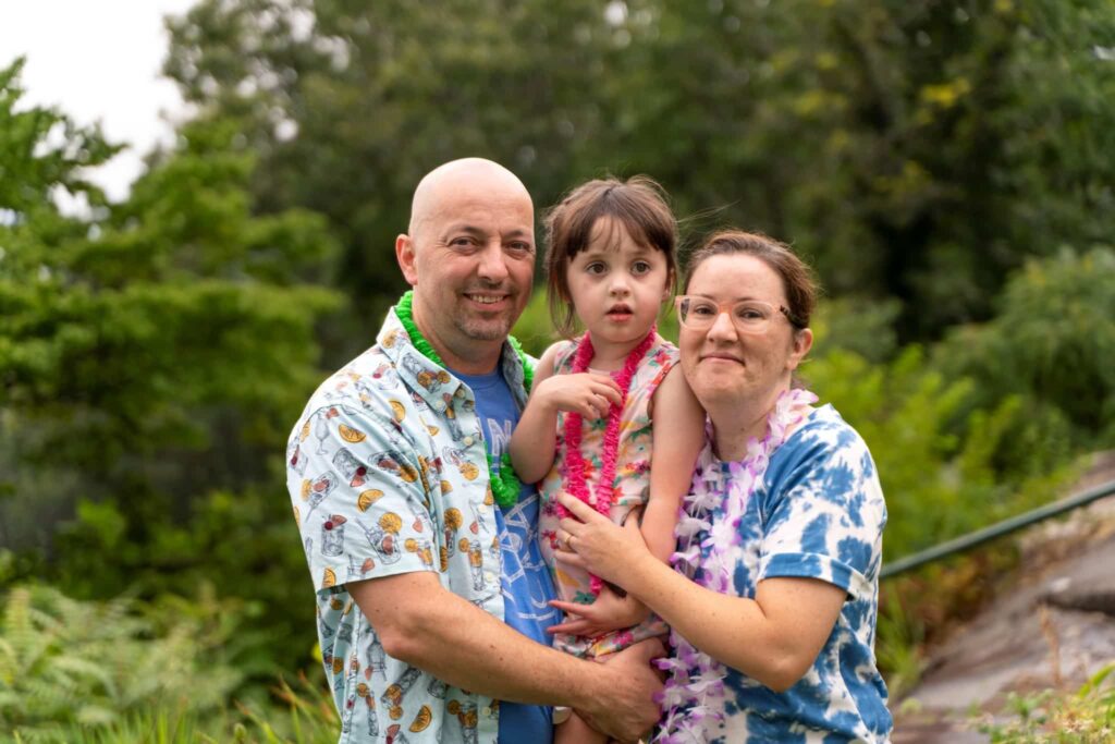 Annabelle's parents, Niki and Jason, holding her between them as they smile at the camera.