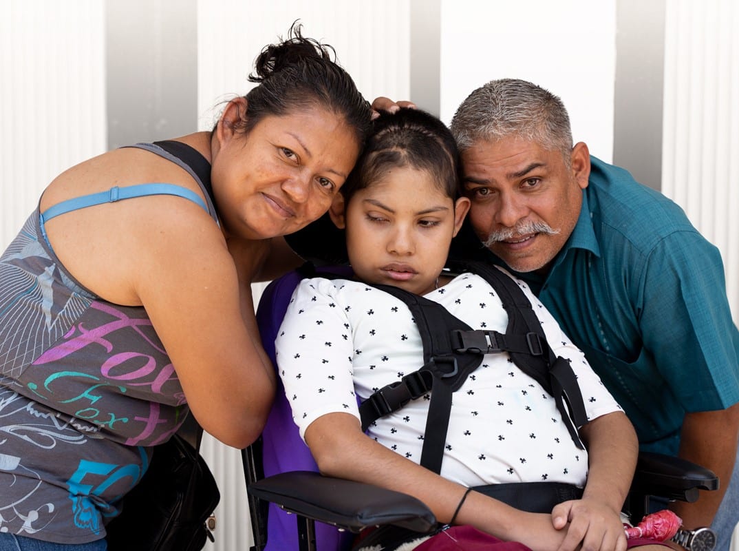 Liz with her mother and her father on either side of her as she's seated in her new wheelchair.