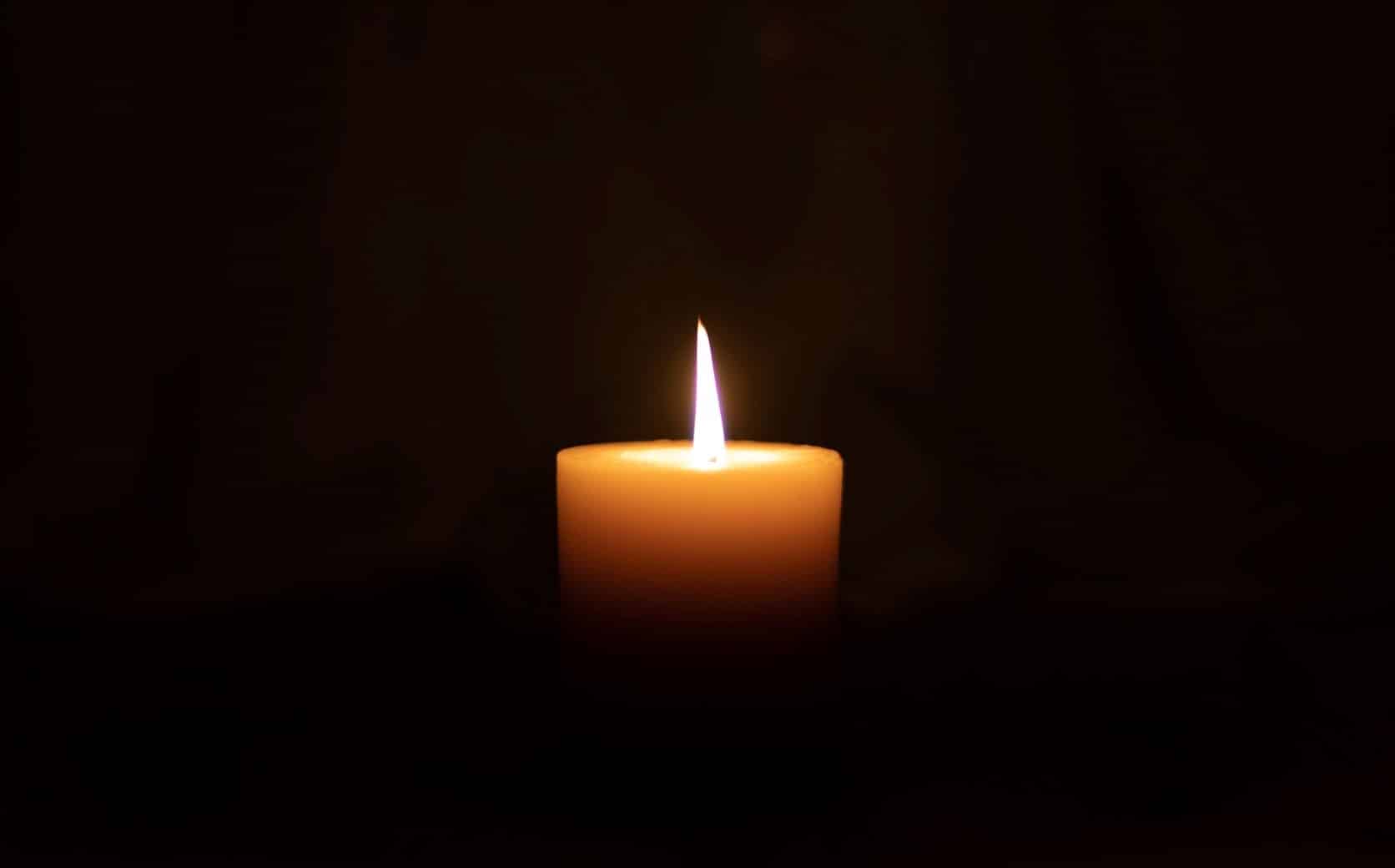 Close up of a lit candle in the middle of a dark room.