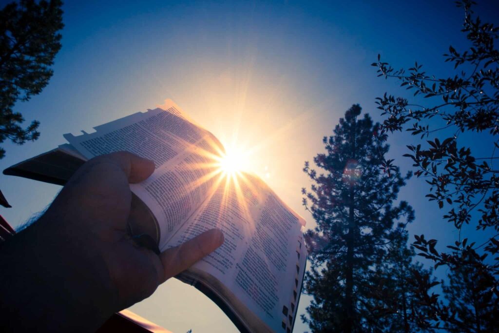 A man holding a bible up in the sky in front of the sun.