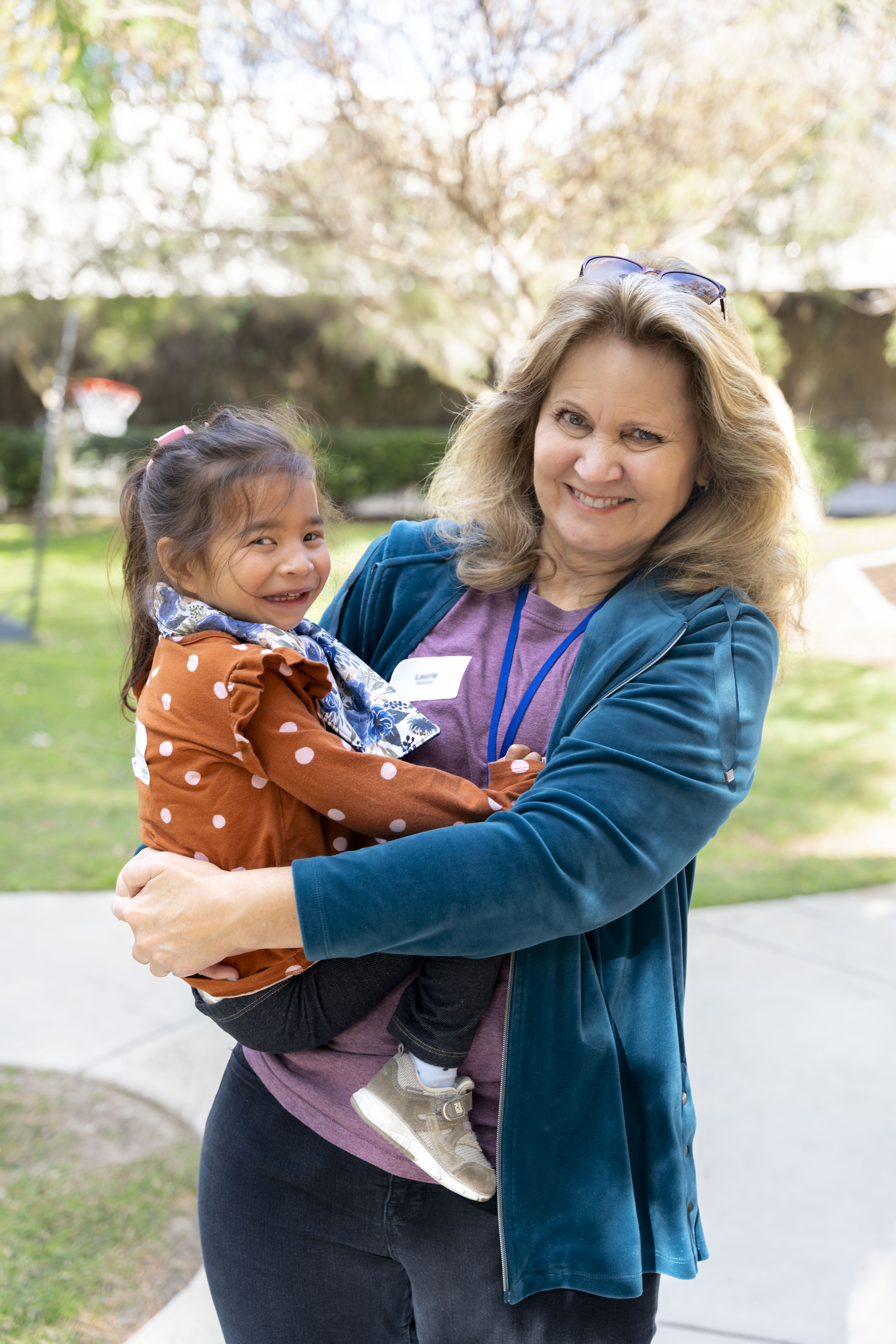 A woman smiling at the camera as she holds her little buddy in her arms who is also smiling at the camera.