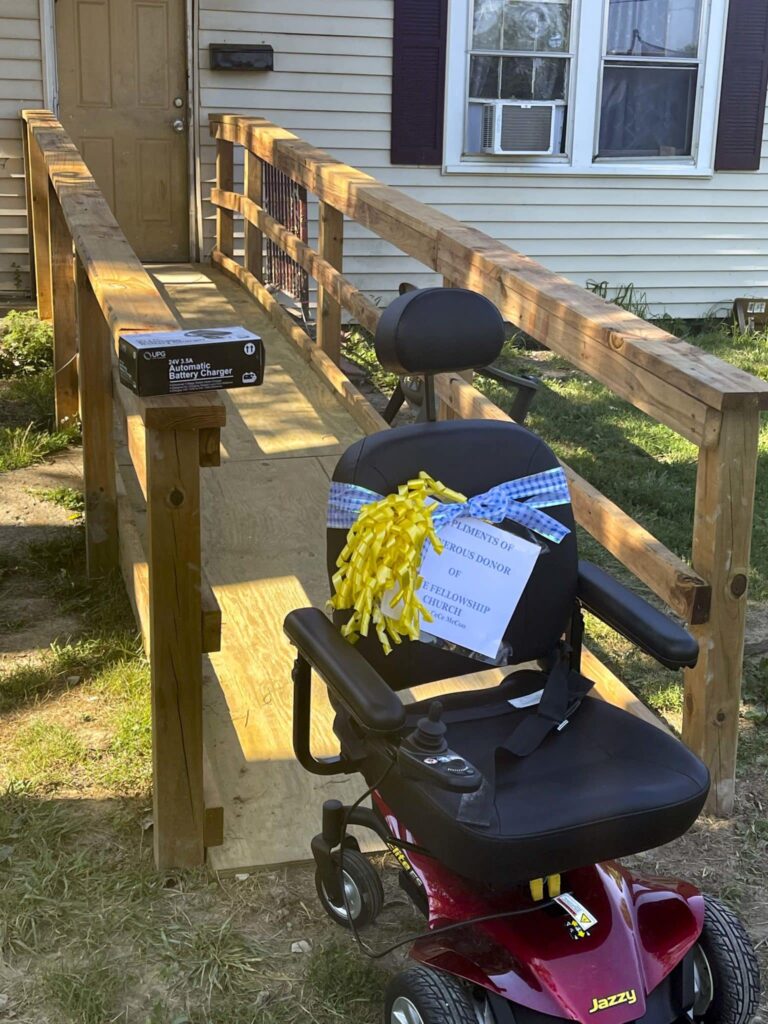 A photo of Anthony's new wheelchair with ribbon on it, in front of the new front door ramp outside of Anthony's home.
