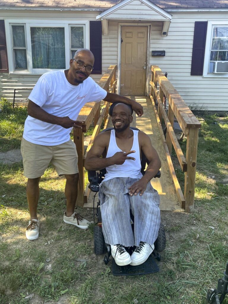 Kempton Turner (left) posing for a picture with Anthony (right) seated in his wheelchair, in front of the new front door ramp outside of Anthony's home.