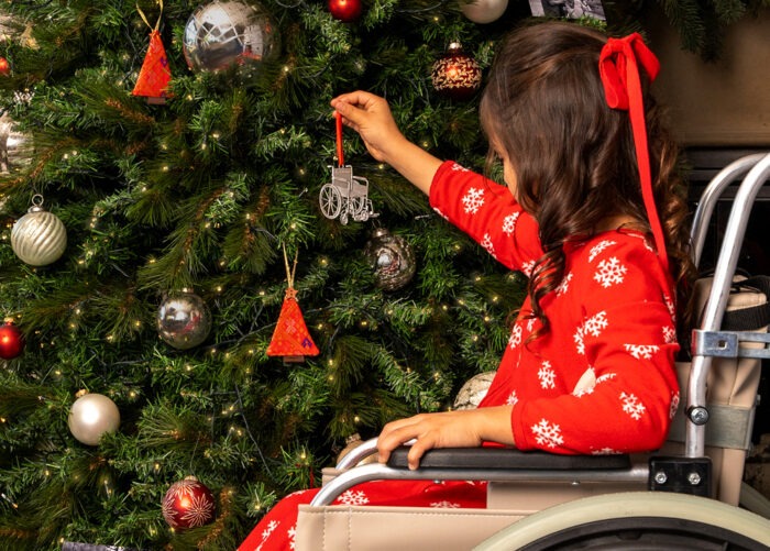 A girl in her wheelchair hanging the wheelchair ornament on a Christmas tree
