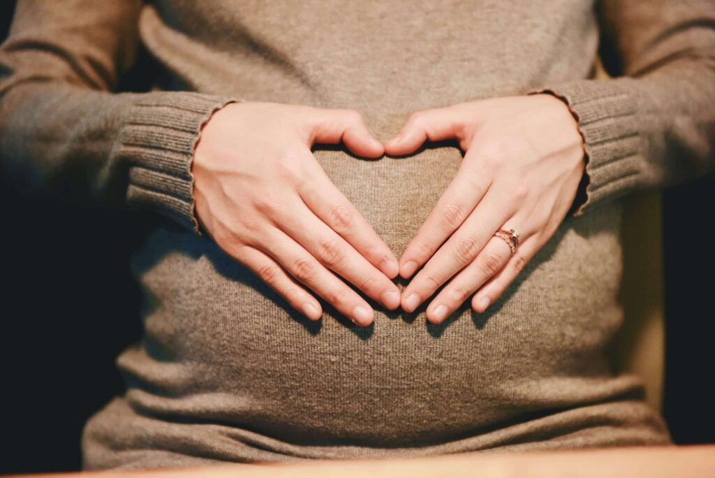 Close up of a woman placing her hands over her pregnant belly in the shape of a heart.
