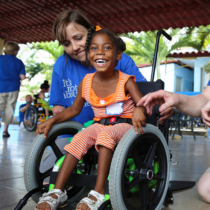 A volunteer check for a proper fit. The child smiles in her new wheelchair.