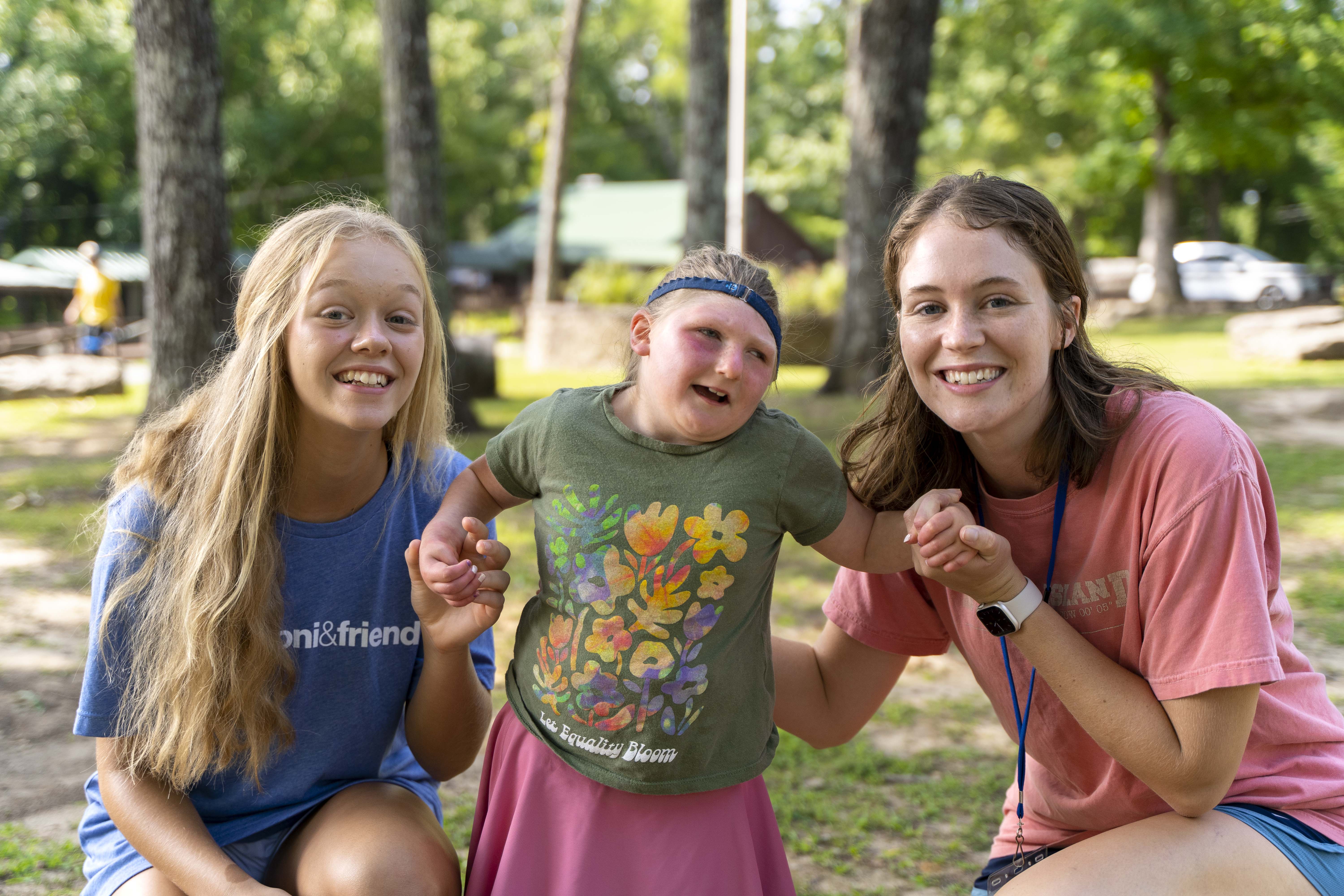 Two young women Joni and Friends volunteers with a young girl with a disability helping her stand.