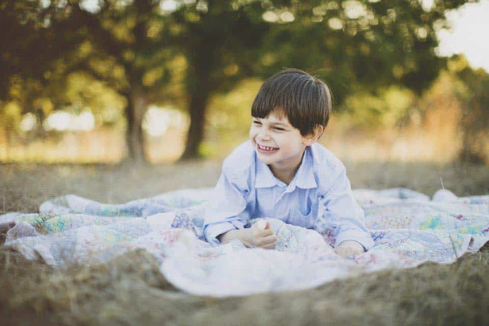 Young Isaac smiling as he lays on a blanket on the grass.