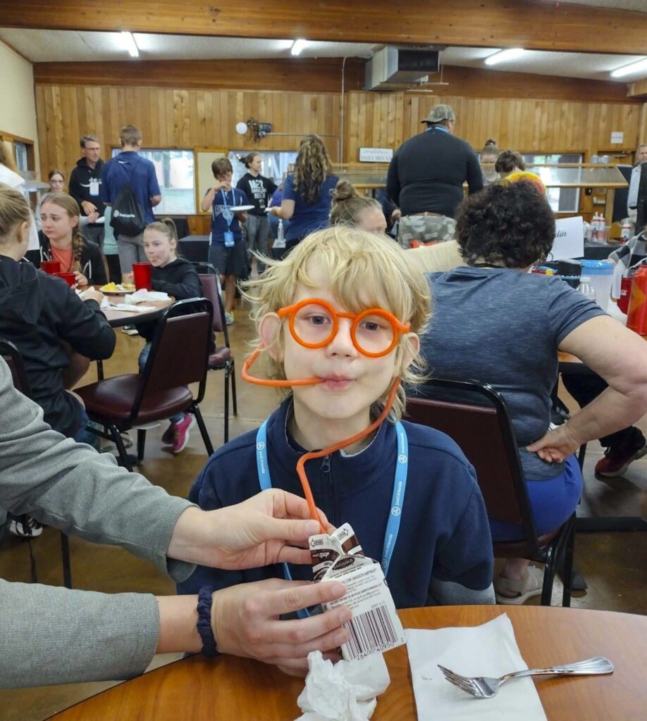 One of Sarah and Allen's boys with orange-rimmed glasses on and a stretchy straw in his mouth as he's drinking chocolate milk.