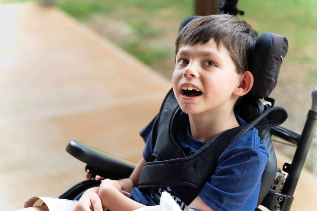 A little boy in a wheelchair smiling up at the camera.