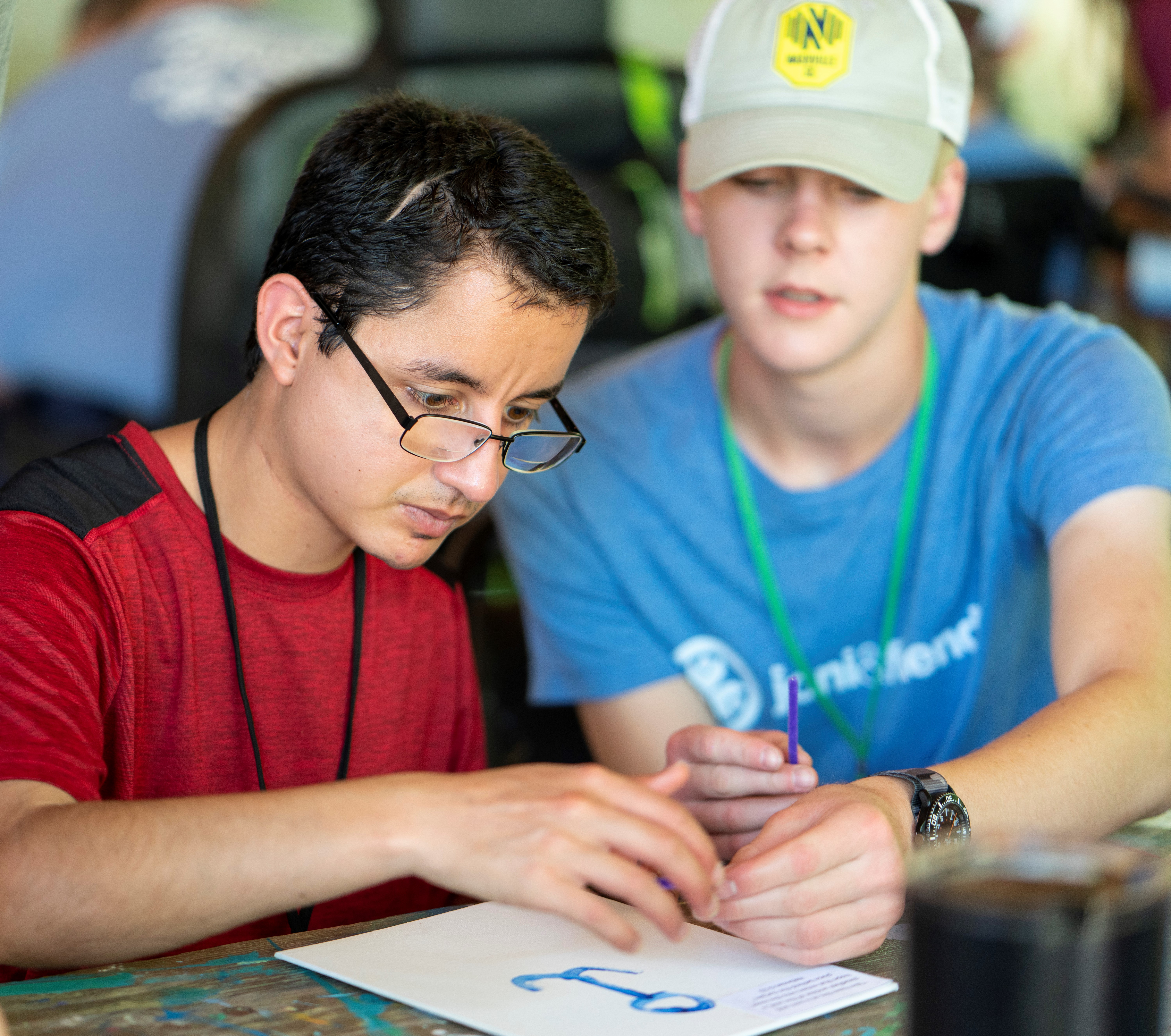 A young man with a disability painting with a Joni and Friends volunteer sitting next to him and helping him.