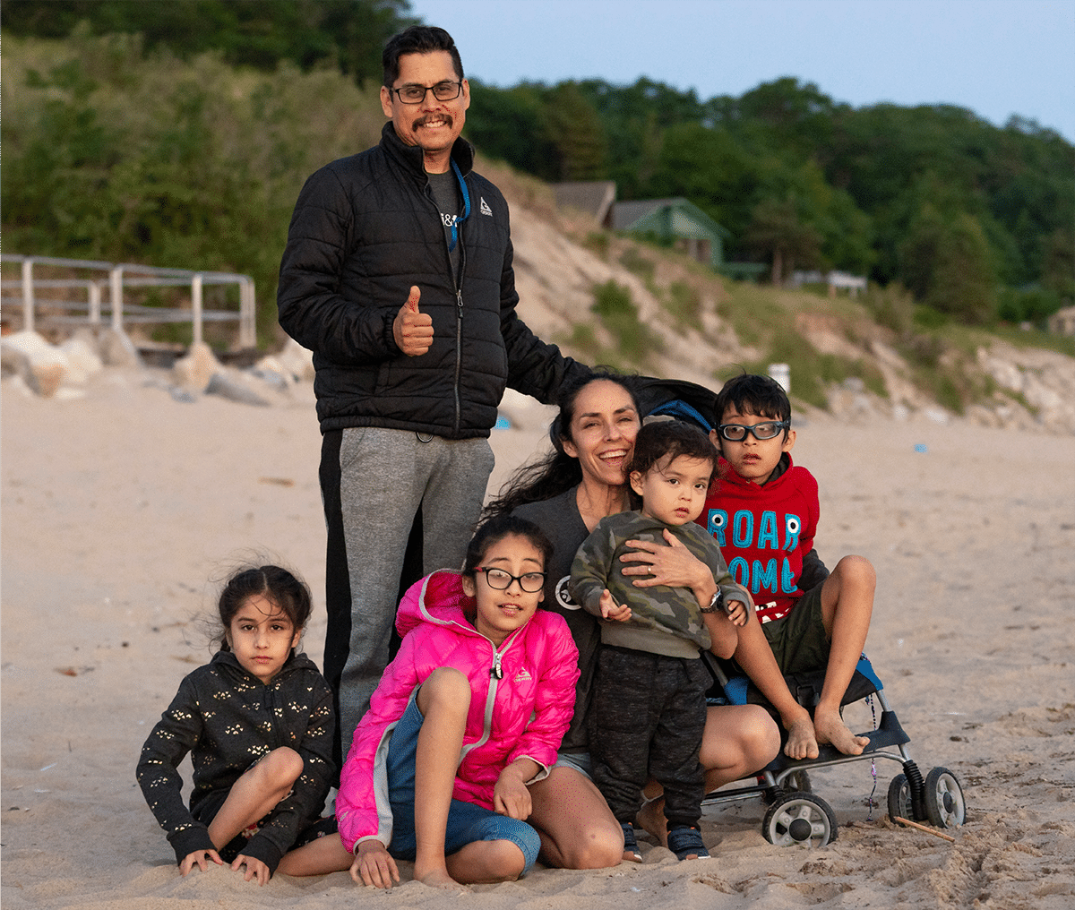 The Rojas family at the beach sitting on the sand, all smiling at the camera.
