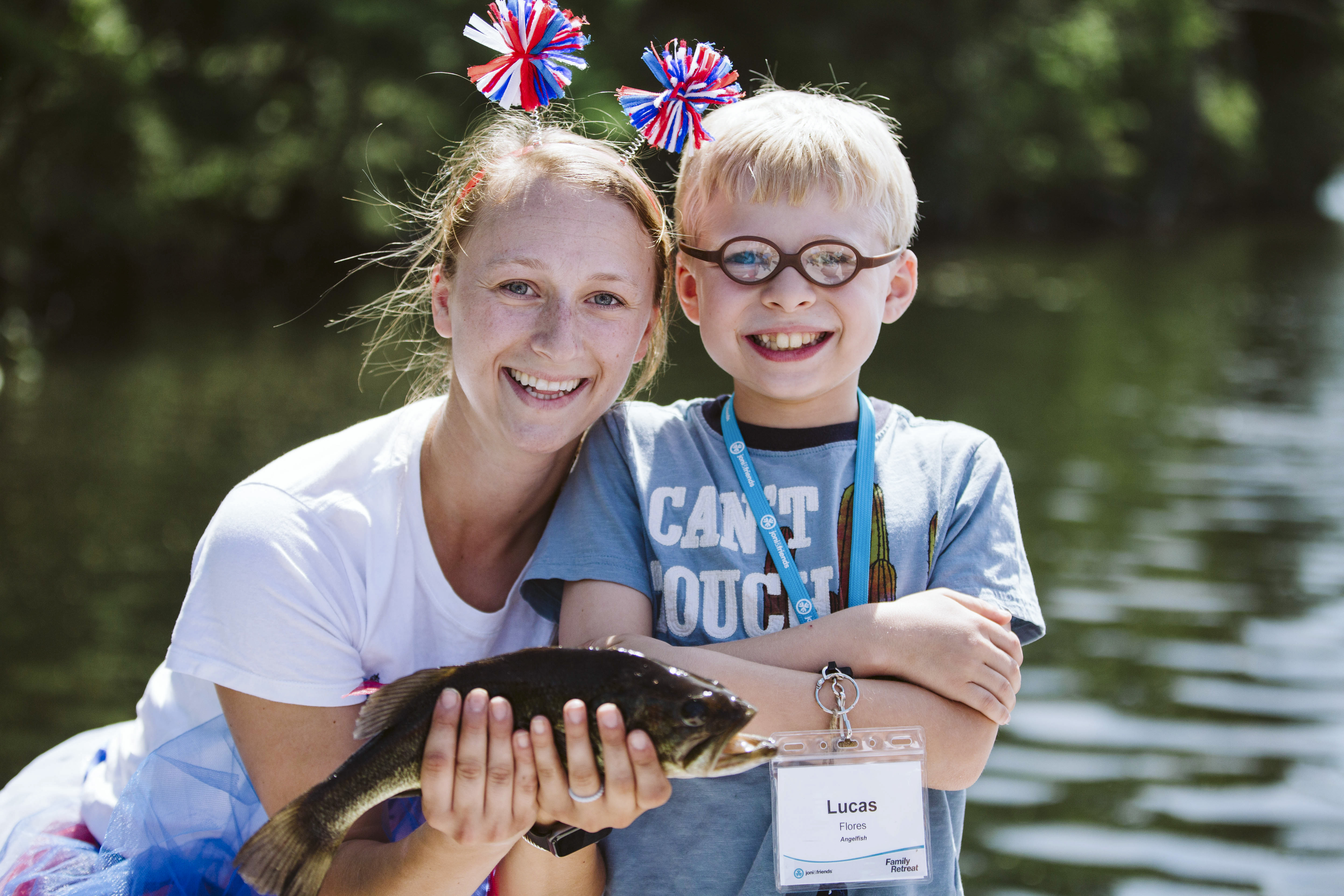 A little boy with glasses on next to a young woman holding a fish and wearing a headband.