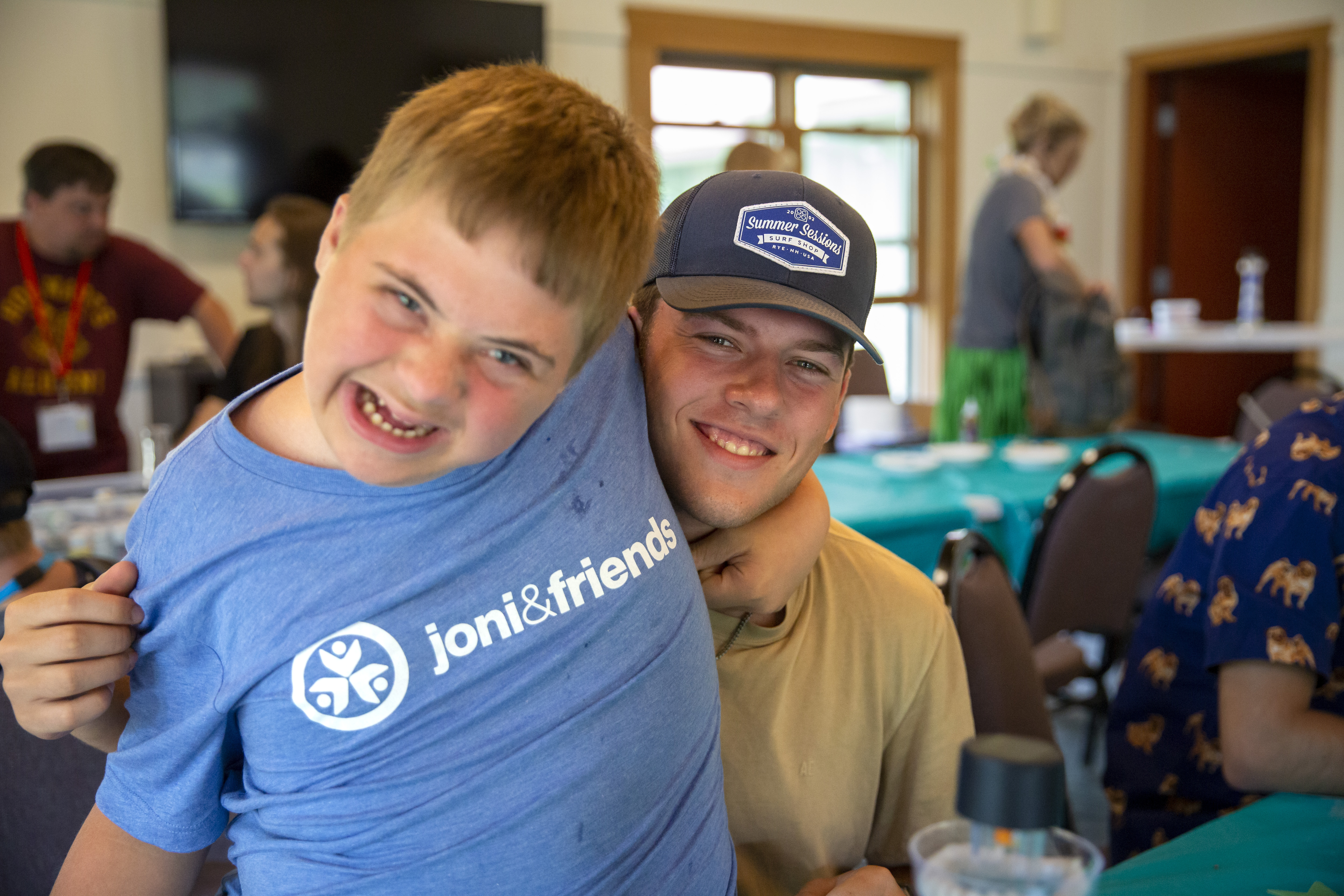 A young boy with a disability growling at the camera and a young man hugging him and smiling at the camera.