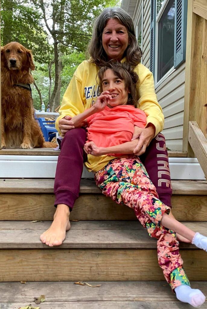 Kate and Laura a mother and her daughter smiling, on a porch with a dog.