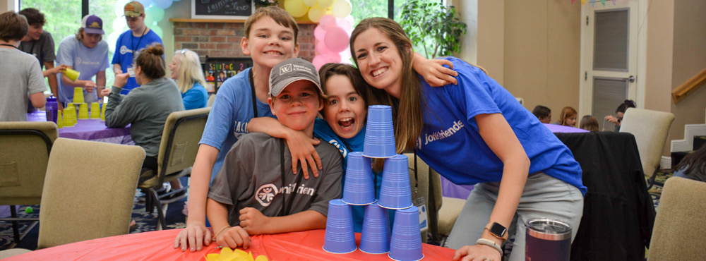 A group of boys with and adult volunteer are having fun doing a cup stacking challenge at Sibling Getaway.