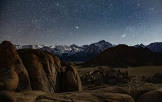 The view of a mountain range in the desert with snow powdering it and a starry sky.