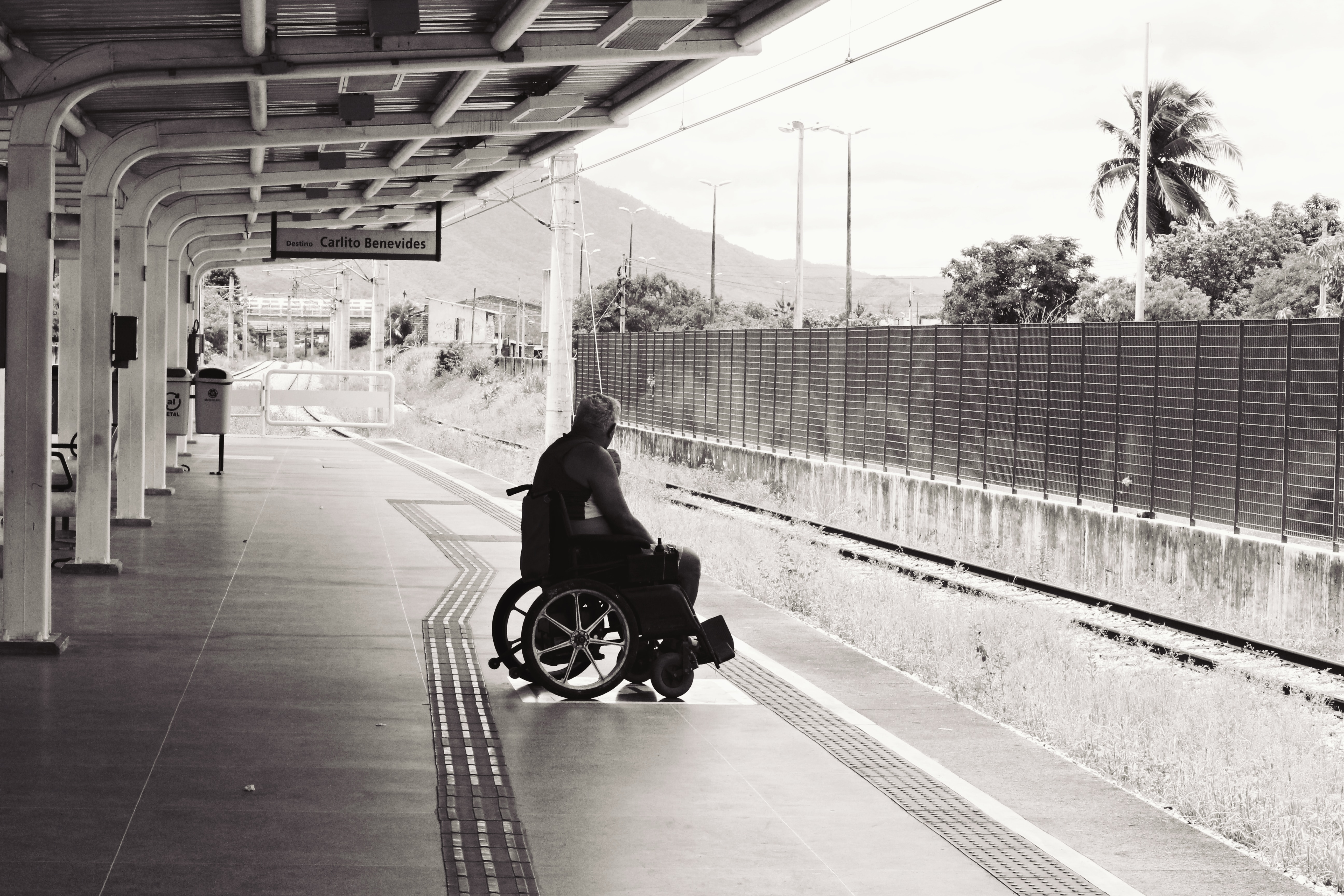 A man seated in a wheelchair beside what looks like a train station.