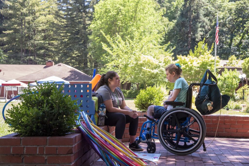 A picture of Cathryn seated in her wheelchair across from a Joni and Friends volunteer as they're chatting.