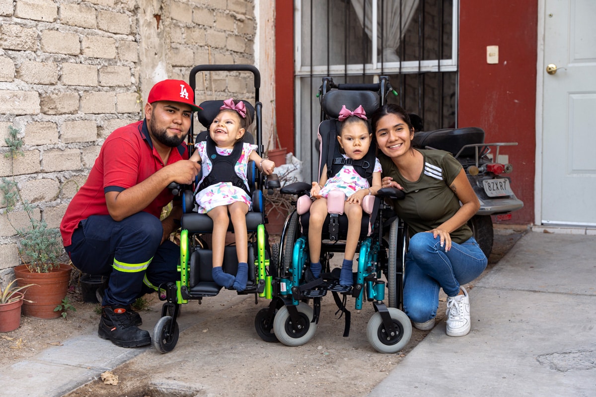 Twins Renatta and Melany in their new wheelchairs with their dad on their left and their mom on their right in front of their house.