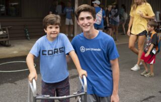 A boy with his walker and a volunteer pose for a photo at Family Retreat