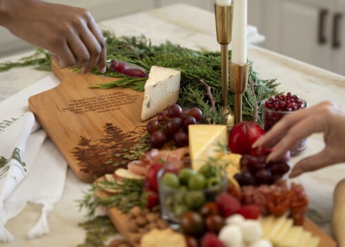 Hands pick at a charcuterie board using the Majestic Mountain cutting board and tea towel set