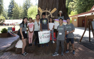 Andrea and her family smiling at the camera in front of a large tree at Bay Area Family Retreat.