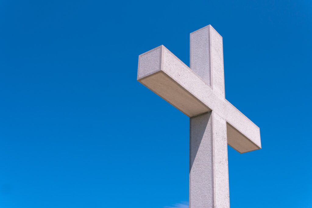 The view from below a white cross with a blue sky background.