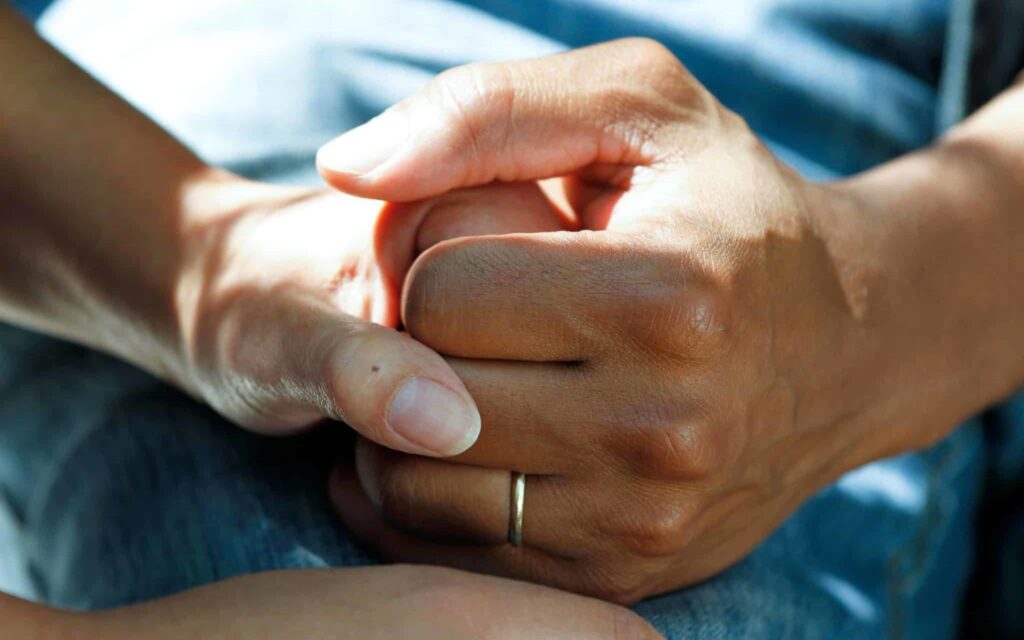 Close up of a man's hand with a wedding ring on holding a woman's hand.