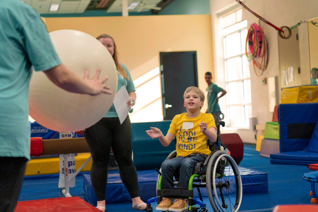 A little boy in a wheelchair tossing an exercise ball back and forth with a Joni and Friends volunteer.