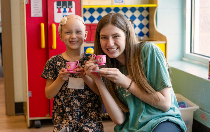 A little girl and her Joni and Friends buddy smiling at the camera as they hold teacups with princesses on them.