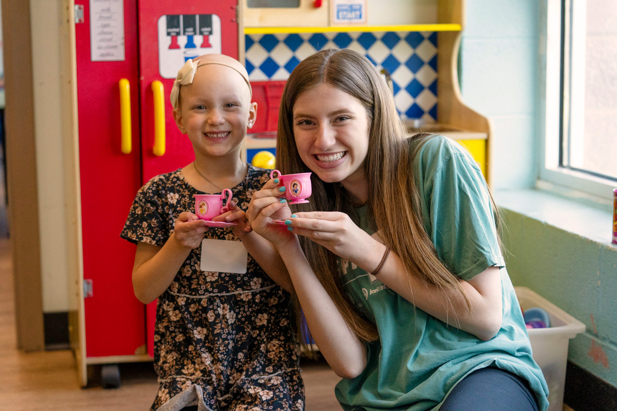 A little girl and her Joni and Friends buddy smiling at the camera as they hold teacups with princesses on them.