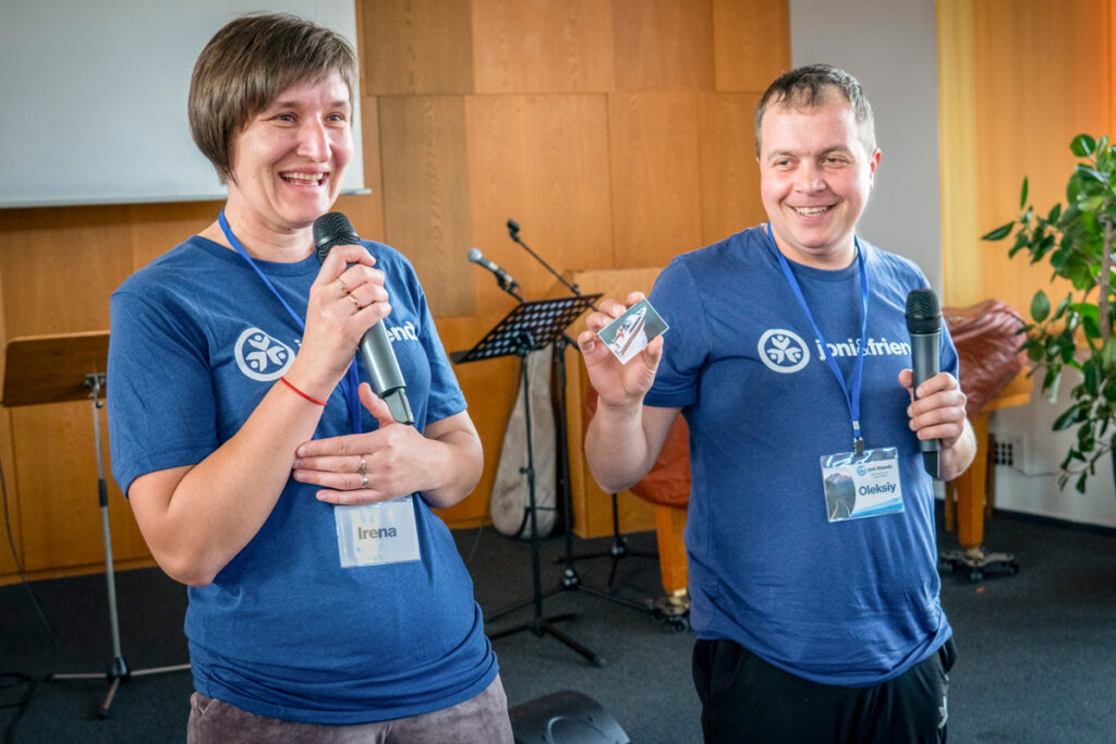 Irena and her husband Oleksiy on stage with their blue Joni and Friends shirts on, smiling as they hold microphones in their hands.