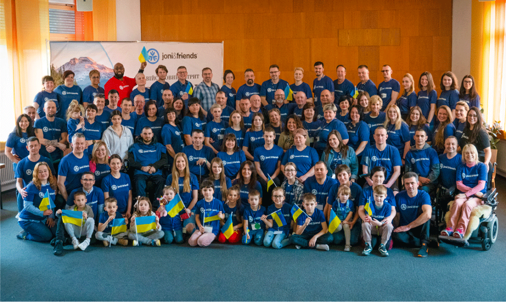 Group photo of volunteers and attendees at Ukrainian Warrior Getaway smiling at the camera with their blue Joni and Friends shirts on.