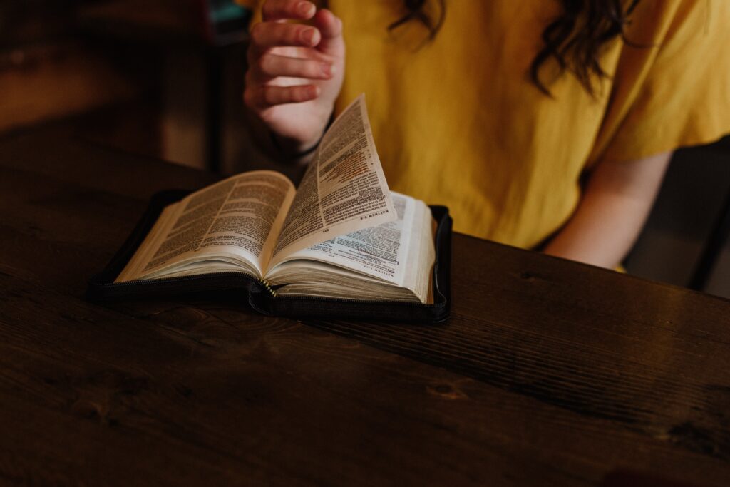A woman flipping through her Bible that's sitting on a wooden table.