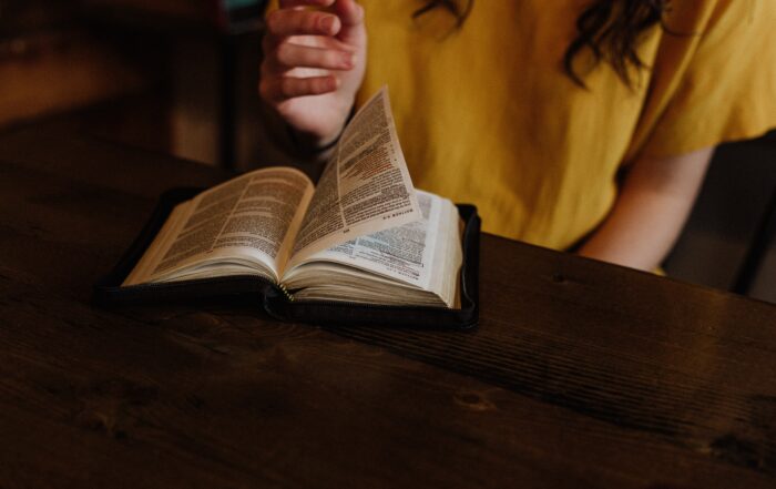 A woman flipping through her Bible that's sitting on a wooden table.