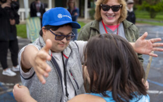 A picture of a young man with Down Syndrome wearing a Joni and Friends hat as he goes in to hug a friend. A woman is standing behind him and smiling.