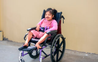 Gaudalupe Maria sitting in her new, perfectly fitted, purple wheelchair smiling wide at the camera.