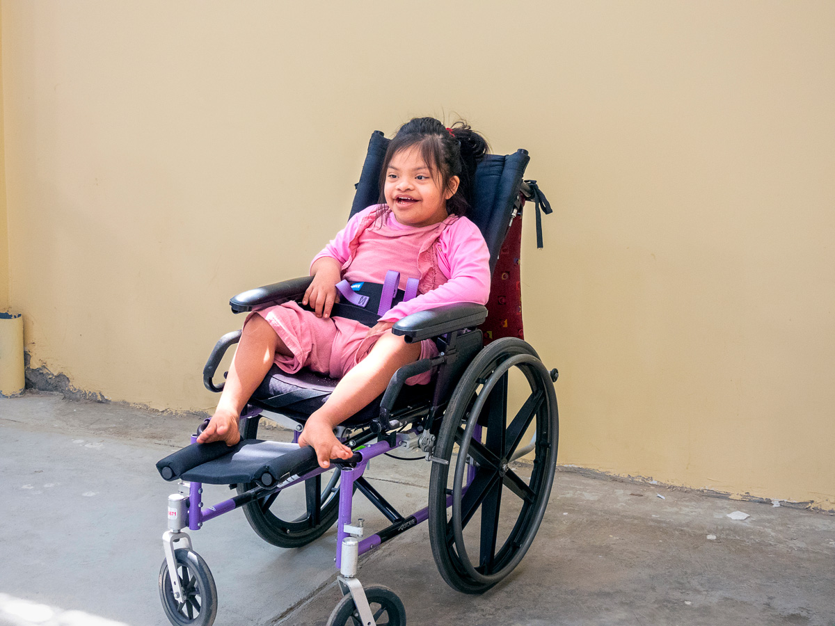 Gaudalupe Maria sitting in her new, perfectly fitted, purple wheelchair smiling wide at the camera.