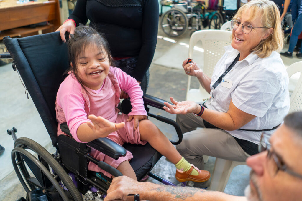 Gaudalupe Maria smiling as she sits in her new wheelchair. She's looking at her nails as a Joni and Friends volunteer gives her a manicure.