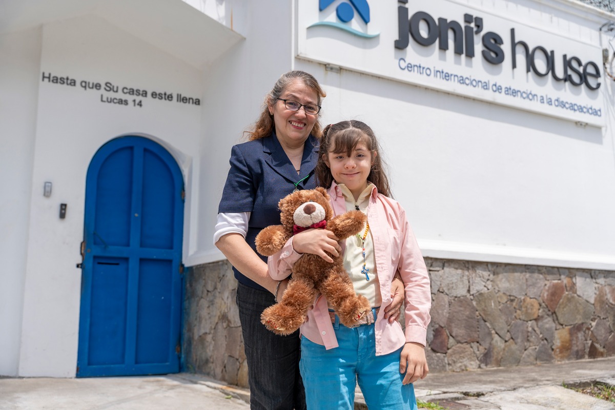 Johanne and her mother Wendy standing next to each other outside of Joni's House smiling at the camera. Johanne has a stuffed bear in her hand.