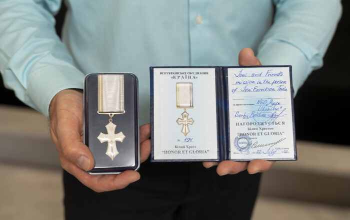 Close up of a man's hands holding up the medal that was awarded and the formal certificate beside it.