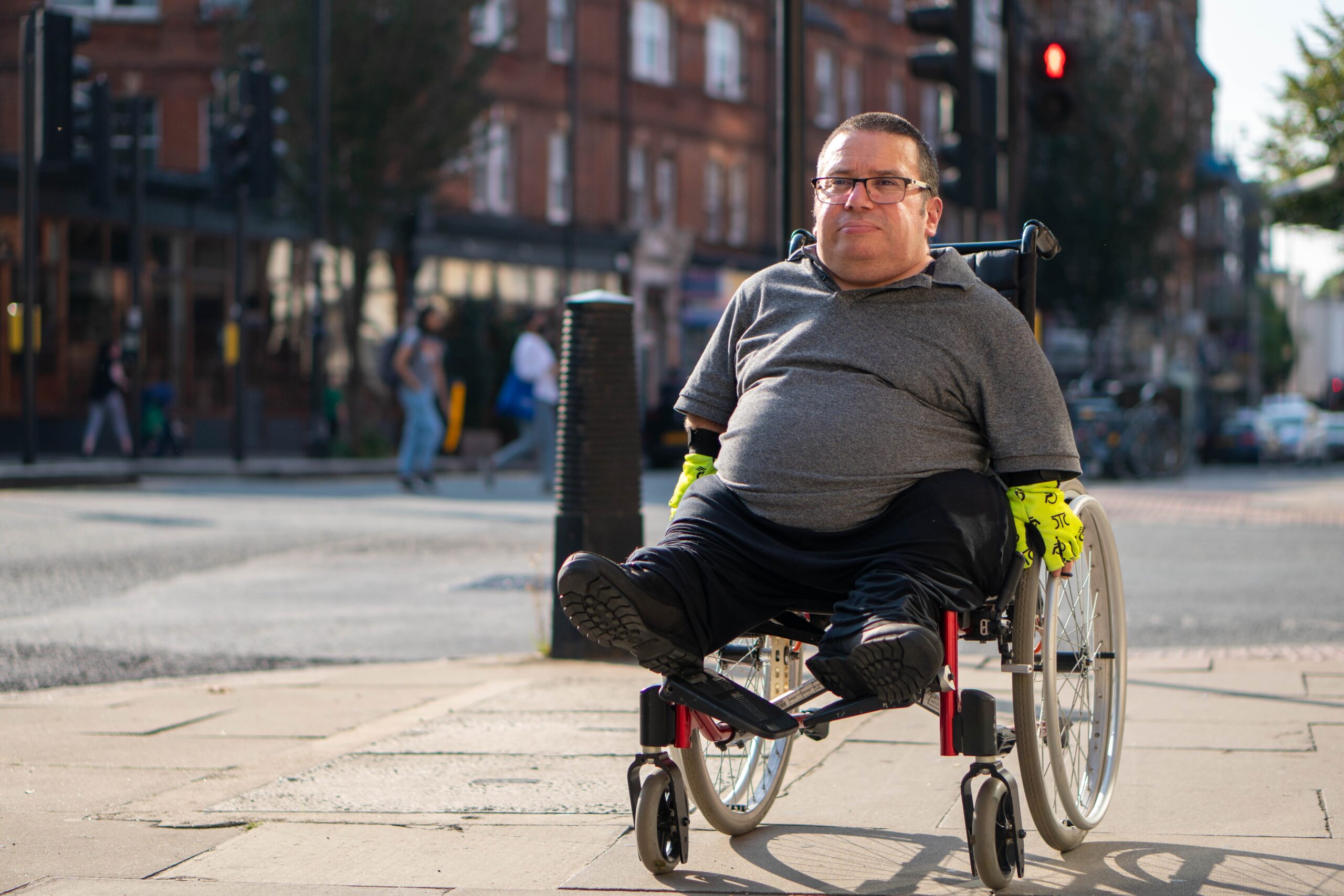 A man seated in a wheelchair on a street corner smiling.