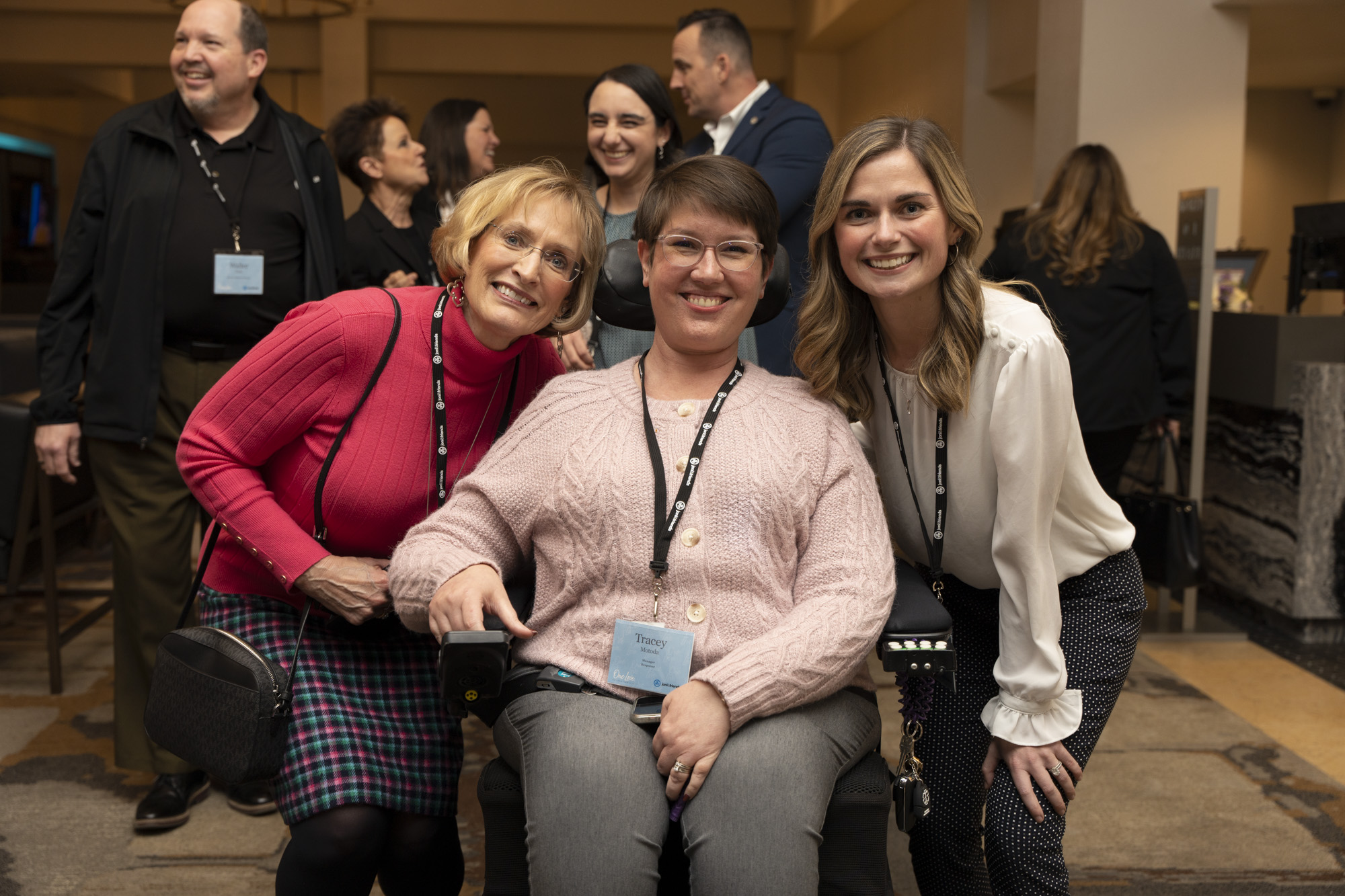 A picture of a woman seated in her wheelchair with to other woman crouching beside her and smiling.