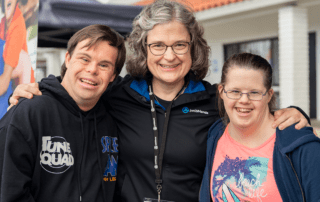 A picture of a Joni and Friends employee with her arms around two people with Down Syndrome as they all face the camera and smile.