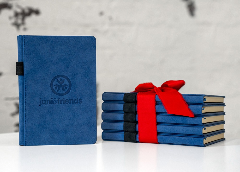 The Joni and Friends Blue Suede Notebooks wrapped in a bow, with one notebook upright showing the front cover